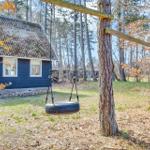 A tire swing hangs between two trees in front of a dark blue house in the woods.
