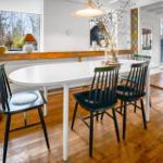 Dining area with white table, black chairs, and wooden floor. Windows with garden view.