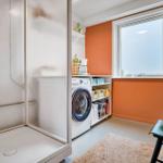 Room with washing machine, window, and closet. Orange wall color and carpet flooring.