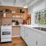 Kitchen with white cabinets, stove, fridge, and window view of forest.