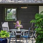 Patio with table, chairs, and flowers in front of a dark wood house.