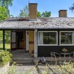 House with terrace, garden, and two chimneys under blue sky.