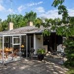 House with glass conservatory, patio, and grill. Surrounded by trees and greenery.