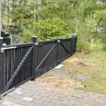 Black wooden gate with driveway and green area in the background.