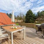 Deck with table, chairs, umbrella, and grill. Background: forest and roof.