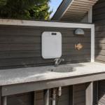 Outdoor sink with countertop, faucet, and cutting board on the wall.