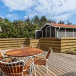Wooden terrace with table and chairs, surrounded by fence and forest.