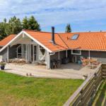 House with wooden terrace, garden, and grill area. Red tiled roof. Terrace with seating.