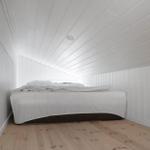 Bedroom with white bed and wooden floor. Walls and ceiling are white clad.