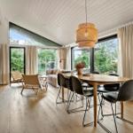 Dining area with wooden table and chairs, adjacent living area with sofa and large windows.
