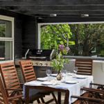 Terrace with table, chairs, grill, and flower arrangement. View of green trees.