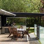 Terrace with grill, table and chairs under a pavilion. Surrounded by trees and a fence.