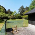 Backyard with play equipment, glass fence, and green lawn. Beside a black-clad house.