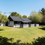 A house with a black roof and white facade, surrounded by grass and trees.