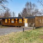 Modern wooden cabin with terrace, garden, and trees in the background.