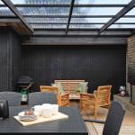 Outdoor area with grill, seating group, and fireplace under glass roof.