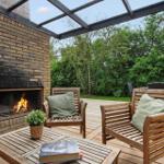Outdoor area with wooden benches, fireplace, and table. Background: green trees.