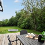 Deck with table, chairs, and plant. Lawn with trampoline and trees in background.