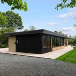Modern villa with wooden terrace and garden. Black facade, large windows.