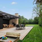 Wooden terrace with seating, grill, table and trampoline in the garden.