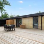 Modern villa with large wooden deck, terrace, and garden table. Surrounded by trees.