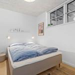 Bedroom with bed, wall shelf, and window. Wooden floor and white walls.