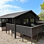 Black wooden house with balcony and windows, surrounded by trees and sand.