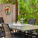 Outdoor area with table and chairs, background with wooden fence and plants.