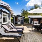 Deck with loungers, table, and umbrella. Background: wooden shed and grill area.