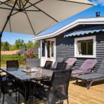 Deck with table, chairs, and umbrella. Background: house with window and lounge chairs.