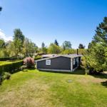 A dark blue holiday home with green lawn and trees in the background.