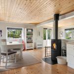 A room with dining area, wooden ceiling, fireplace, and kitchen counter. Windows show garden.