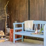 Blue wooden bench with blanket and drink against wood wall. Beside: woodpile and decorative branches.