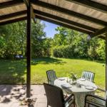 Covered outdoor area with table and chairs. Lawn and trees in the background.