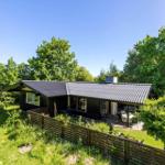 A house with dark cladding and roof, surrounded by greenery and trees. A terrace with table and chairs.