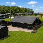 Black wooden cabin with terrace and garden. Surrounded by green lawns and other cabins.