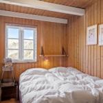 Bedroom with wooden walls, bed, and window. Two pictures hang on the wall.