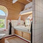 Bathroom with double sink, wooden ceiling, and bathroom window with view of greenery.
