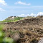Green and brown hills under blue sky with white clouds.