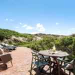 Terrace with table, chairs, and loungers. View of greenery and sky.