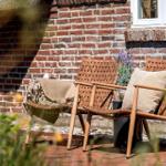 Two chairs with cushions and a blanket stand against a brick wall.
