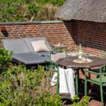 Terrace with seating group, table and chairs next to red brick wall.