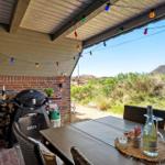 Terrace with grill, table and chairs under colorful string lights. View of green dunes.