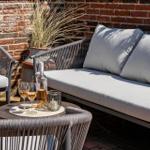 Outdoor area with sofa, chairs, and table. On the table are glasses and a bottle.