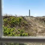 View through a window of a lighthouse behind dunes and grasses.