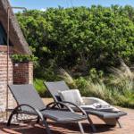 Two lounge chairs on terrace beside house with thatch roof and greenery.