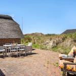 Terrace with table, chairs, and seating areas in front of a thatched roof house.