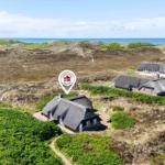 Three houses with thatched roofs are situated on dunes with a view of the sea.