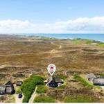 House with thatched roof in dune landscape, view of sea and lighthouse