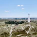 White lighthouse on dunes with view of coastal landscape and sky.